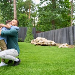 Smiling father hugs his son on the lawn of the house, the boy has a baseball glove